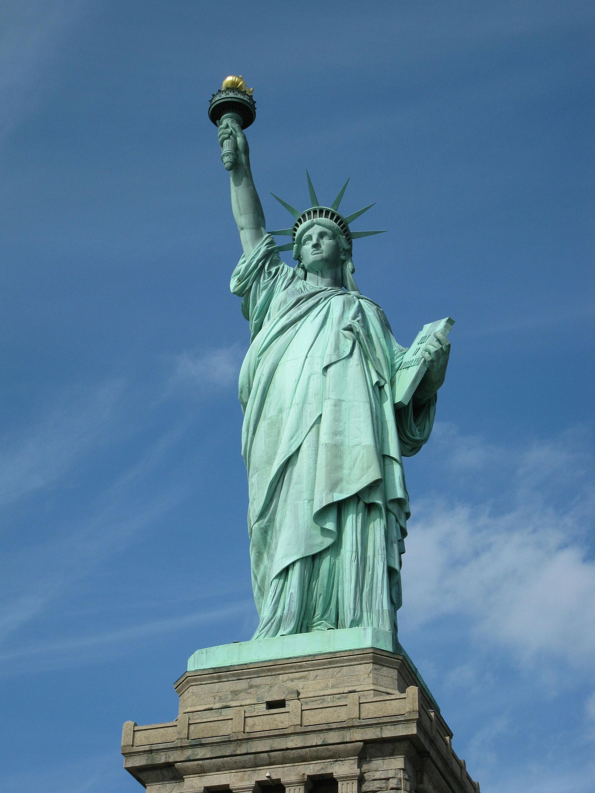 Statue of Liberty, green copper statue on pedestal, holding torch and tablet, blue sky.