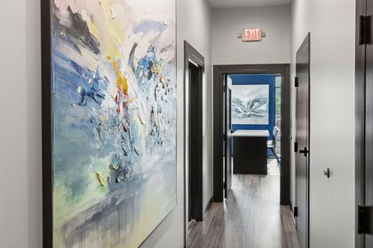Hallway with abstract art, dark door frames, and exit sign. Light wood-look flooring.