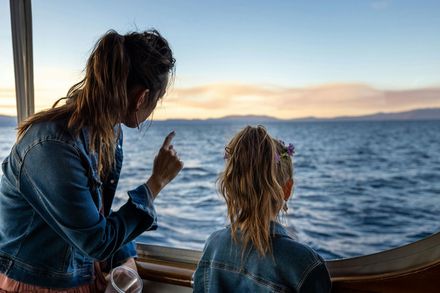 Woman pointing and child looking at the ocean from a boat, during sunset.