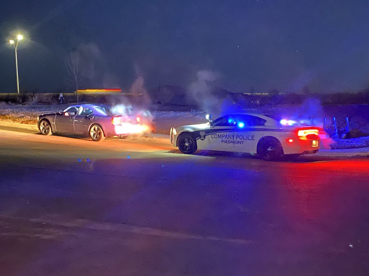 Two police cars with flashing lights stop a dark sedan on a roadside at night.
