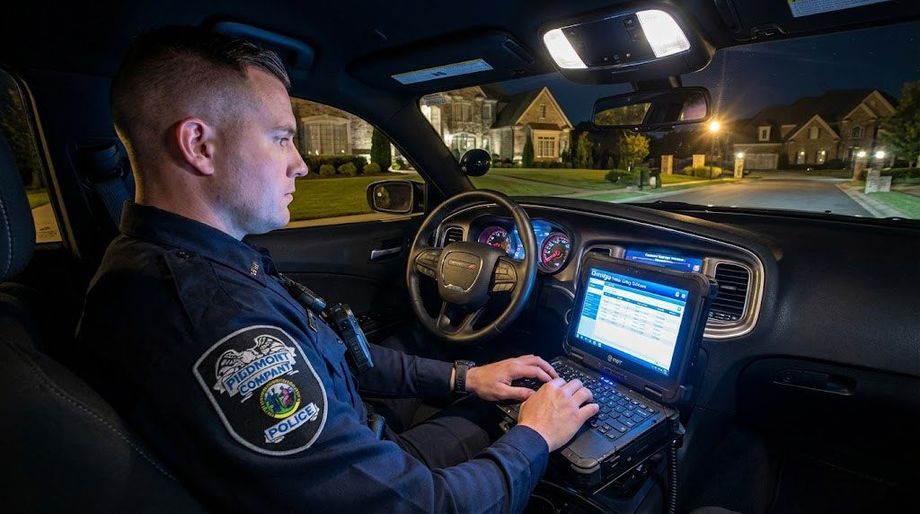 Police cars with flashing lights block a snowy road at night, tire tracks visible in the snow