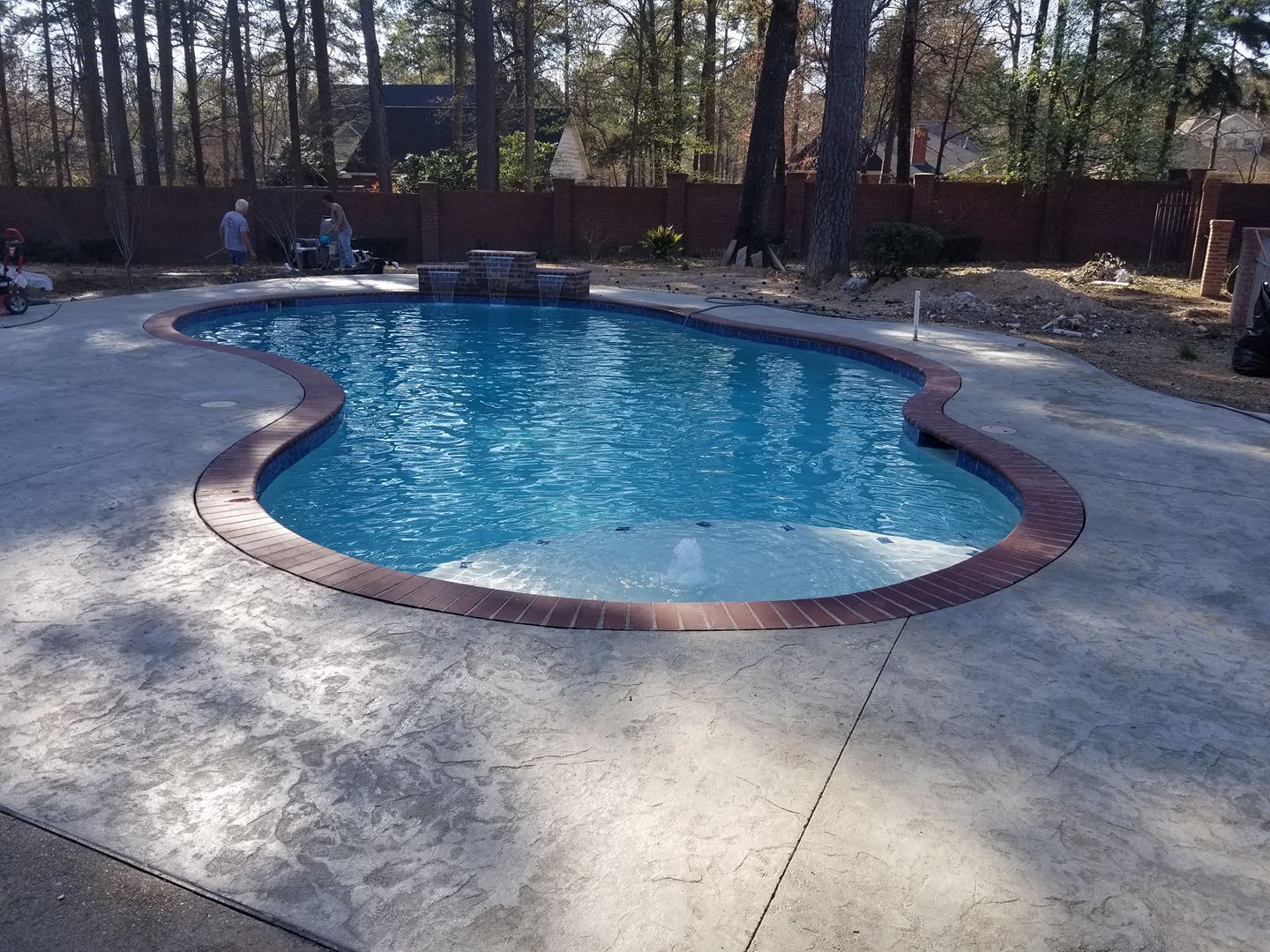 A large swimming pool with a brick border is surrounded by trees in Texarkana, TX