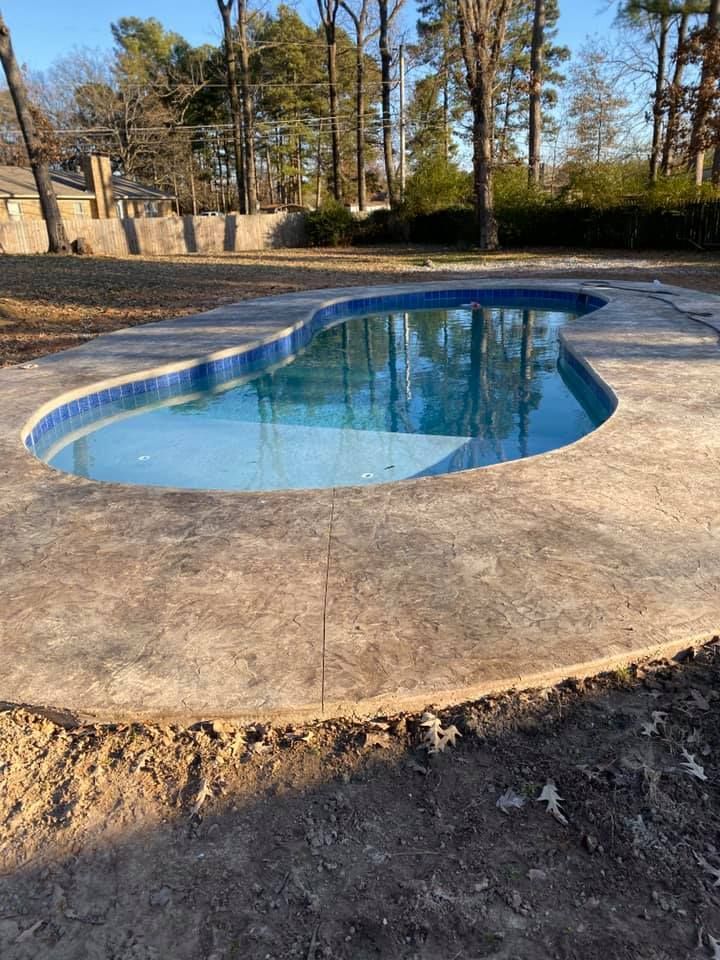 A large swimming pool is surrounded by trees and a concrete deck.