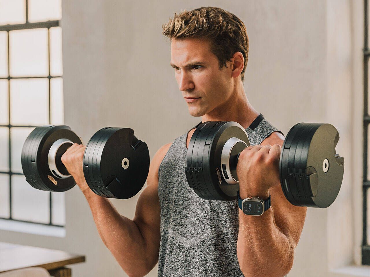 A person performing dumbbell curls in a brightly lit room while wearing a smart watch.