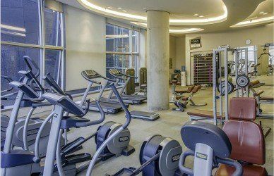 A bright, modern indoor gym featuring rows of elliptical machines, treadmills, and weight equipment on a clean floor.