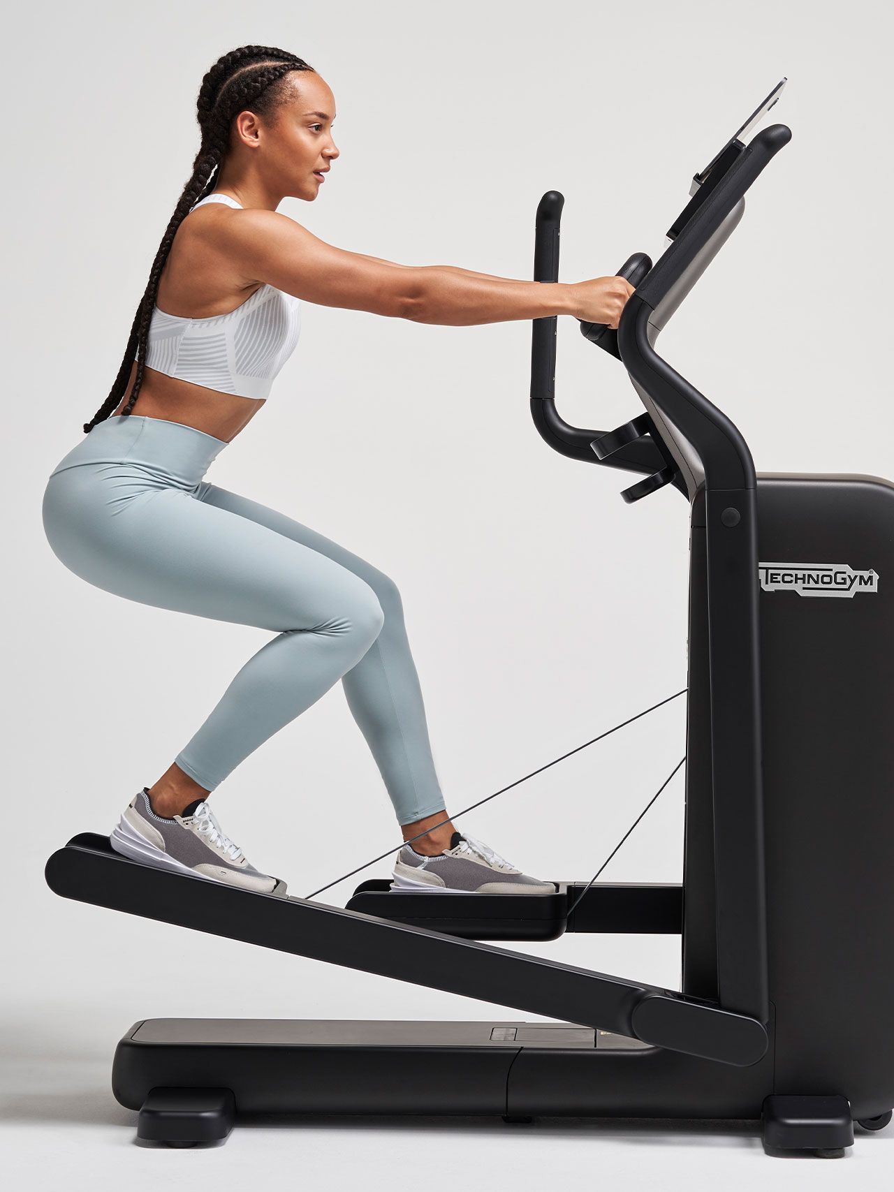 A person in athletic wear performs a squat while using a Technogym exercise machine against a plain white background.