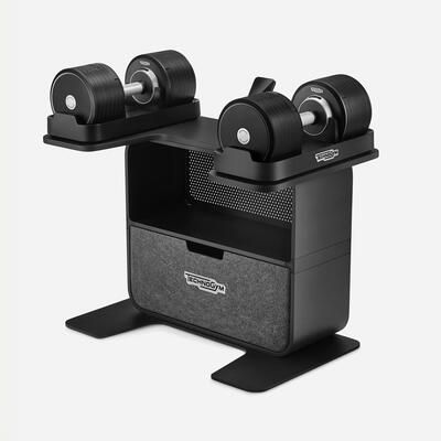 A Technogym rack with a pair of adjustable dumbbells, featuring a storage shelf and drawer in a black finish.