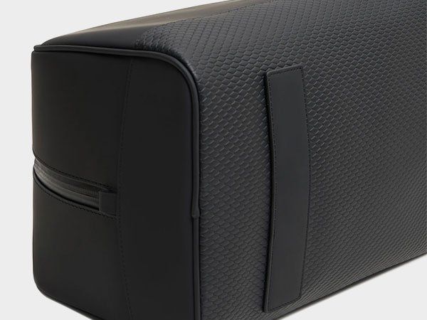 A close-up view of the side of a black bag, featuring a textured pattern and a smooth, vertical leather strap.