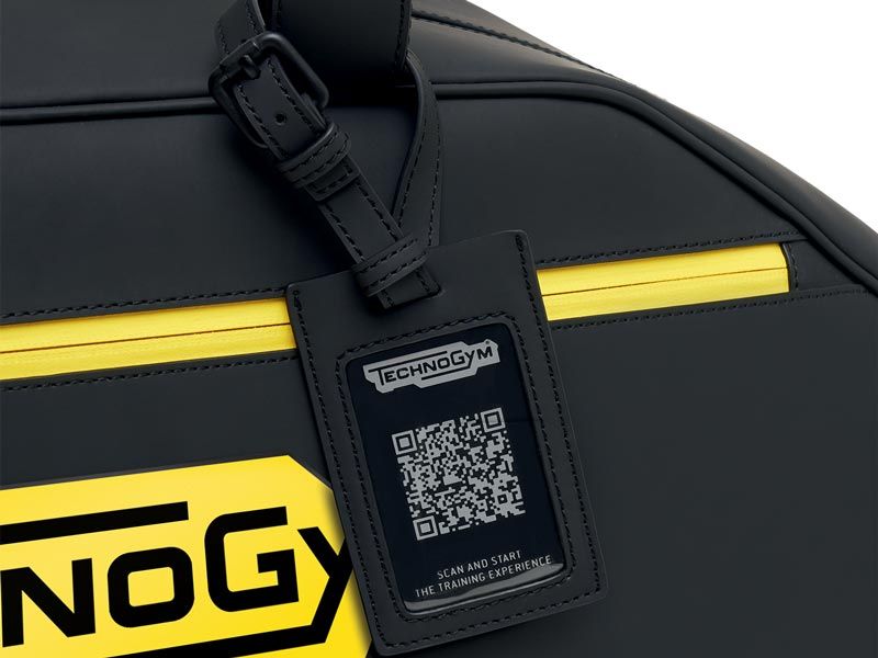 A black bag with a yellow zipper and a Technogym luggage tag featuring a QR code.