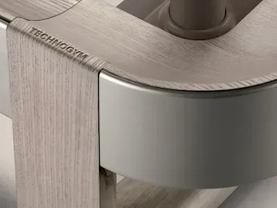 Крупни план Technogym фитнес справе са светлом завршном обрадом дрвета и глатким, мат сивим закривљеним елементом.