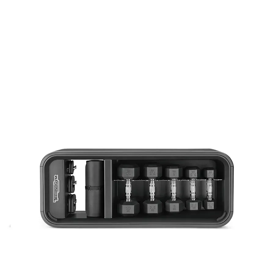 A Technogym storage rack containing five pairs of black dumbbells and other gym accessories, viewed from above.