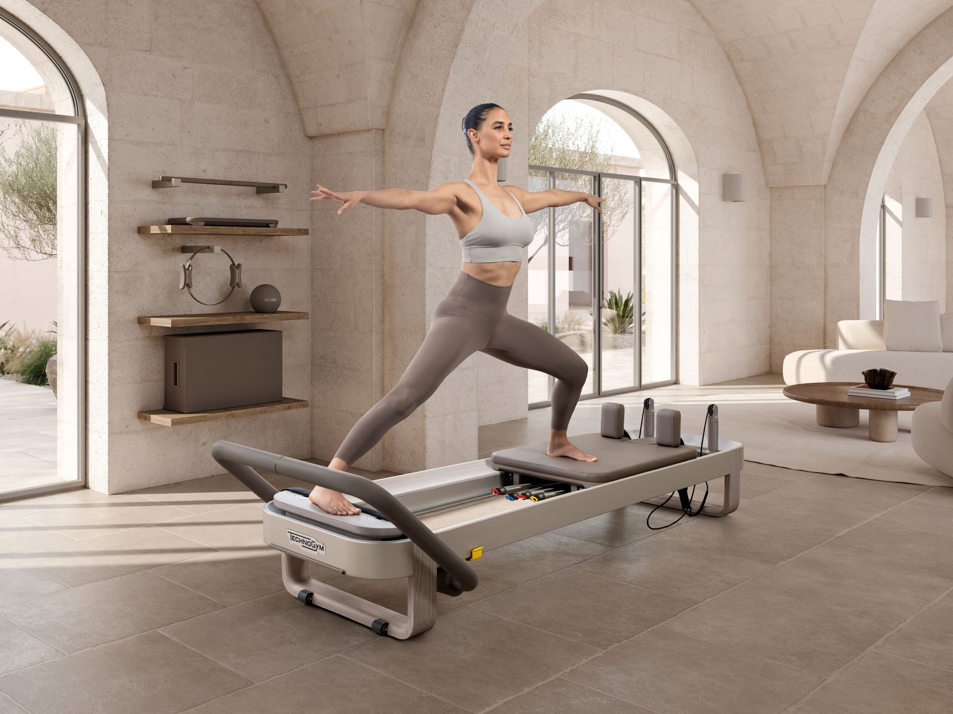 A person performs a Pilates exercise on a reformer machine, sitting on a box with one leg extended vertically.