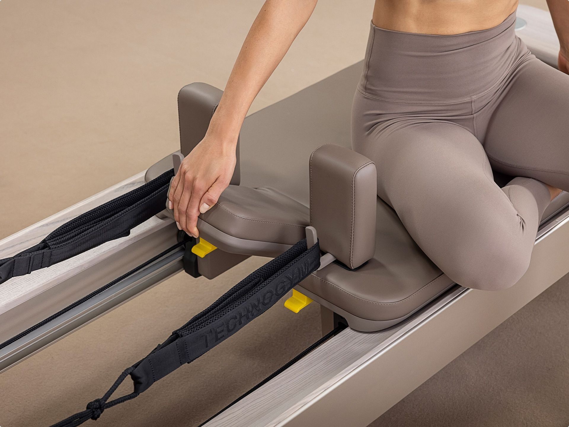A person performs a Pilates exercise on a reformer machine, sitting on a box with one leg extended vertically.