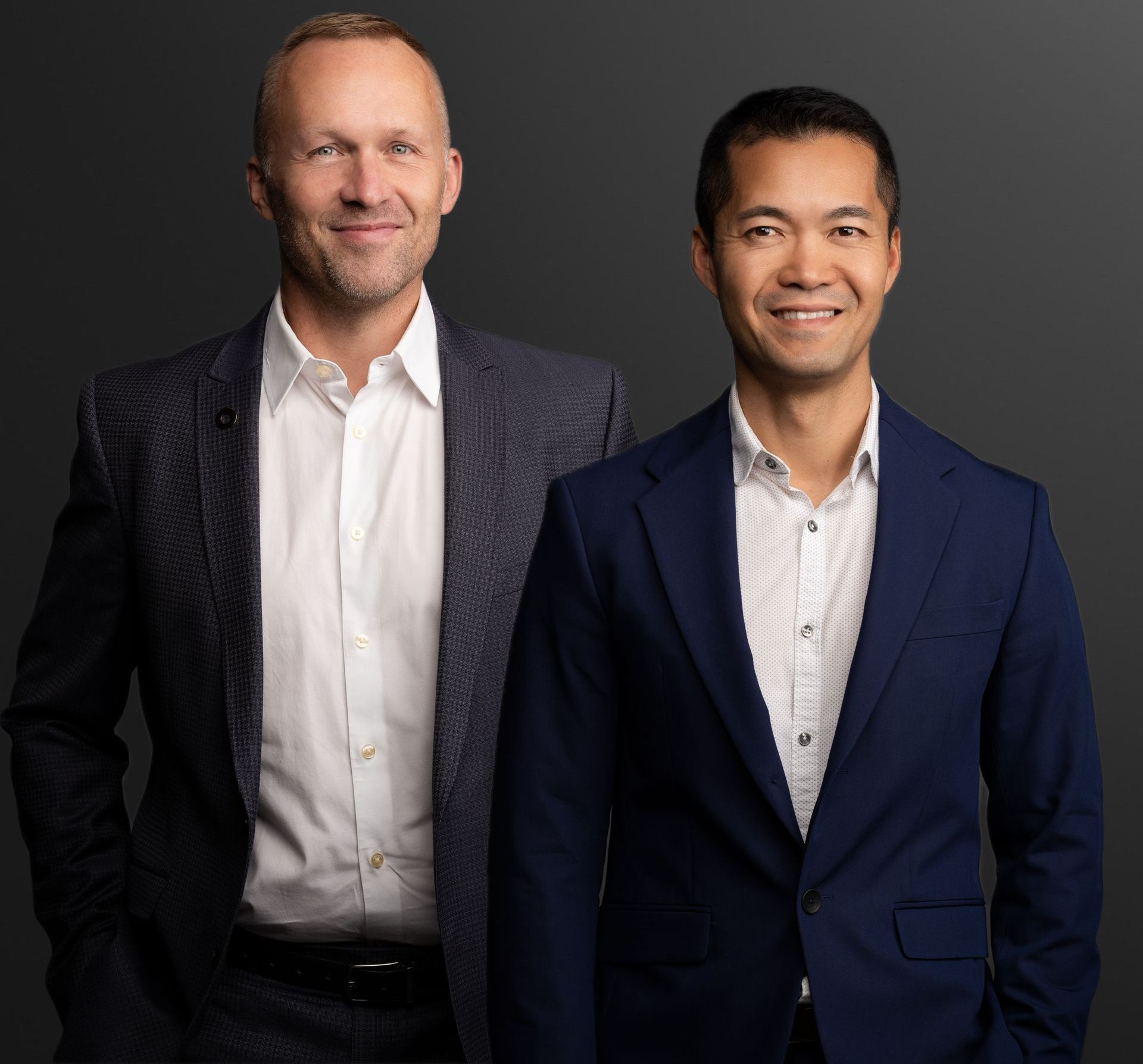 Two men in business suits standing against a dark studio background