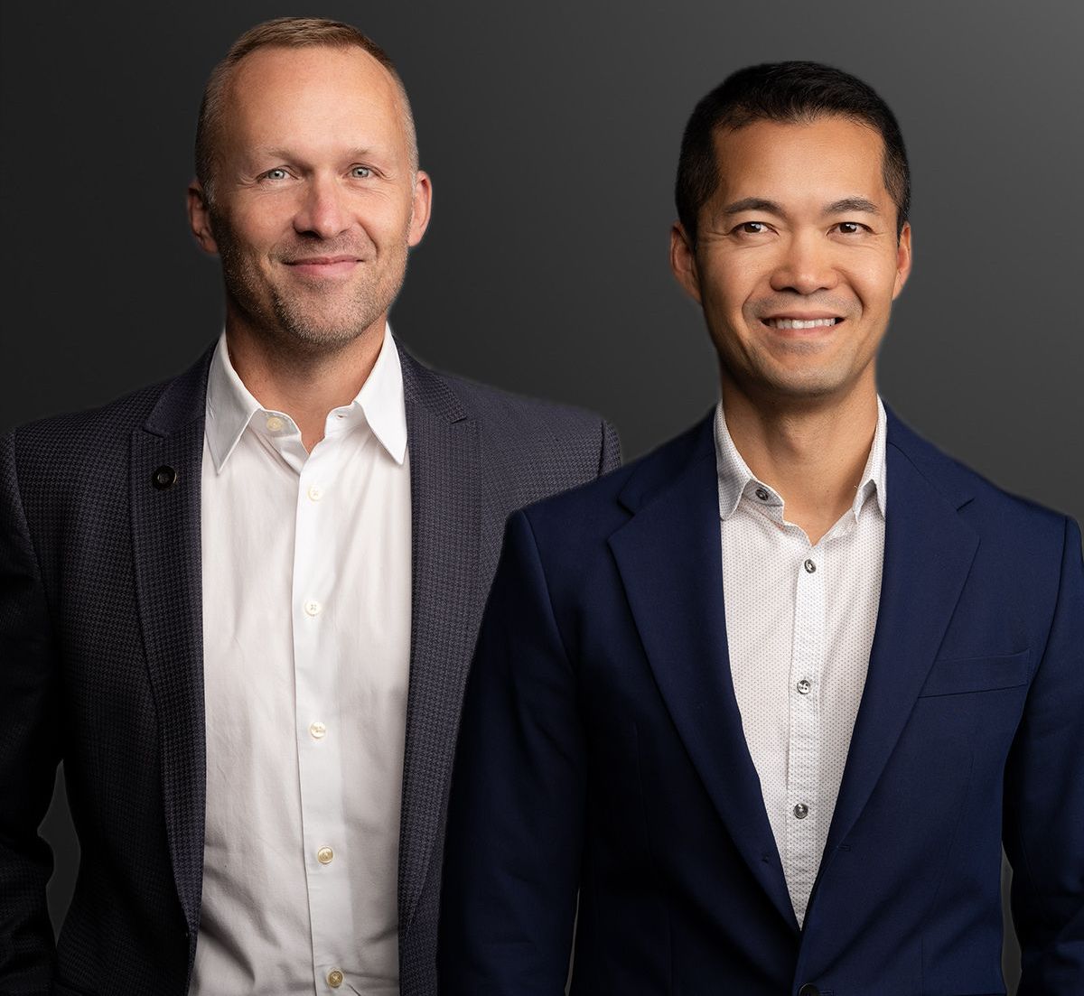 Two men in business suits standing against a dark studio background