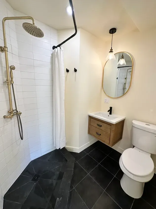 A bathroom with a toilet , sink , shower and mirror.