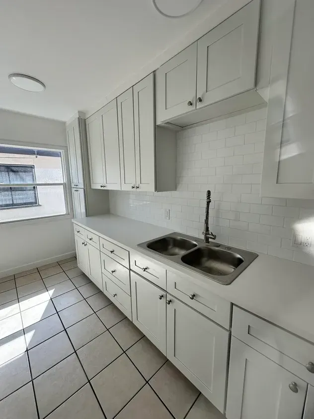 A kitchen with white cabinets , a sink , and a window.