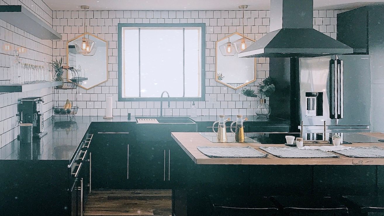 A kitchen with black cabinets , stainless steel appliances , a sink , and a refrigerator.