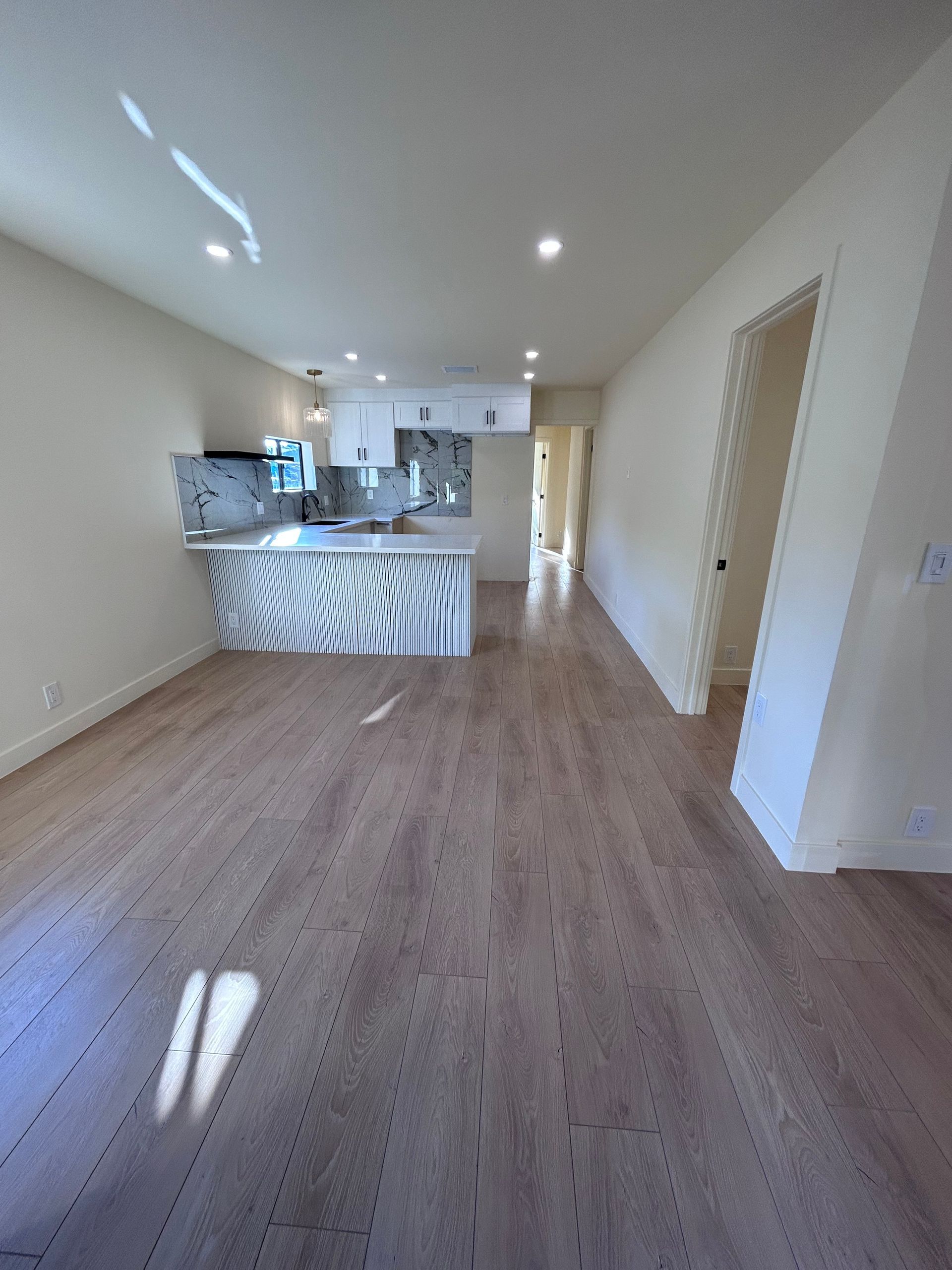 A living room with hardwood floors and a kitchen in the background.