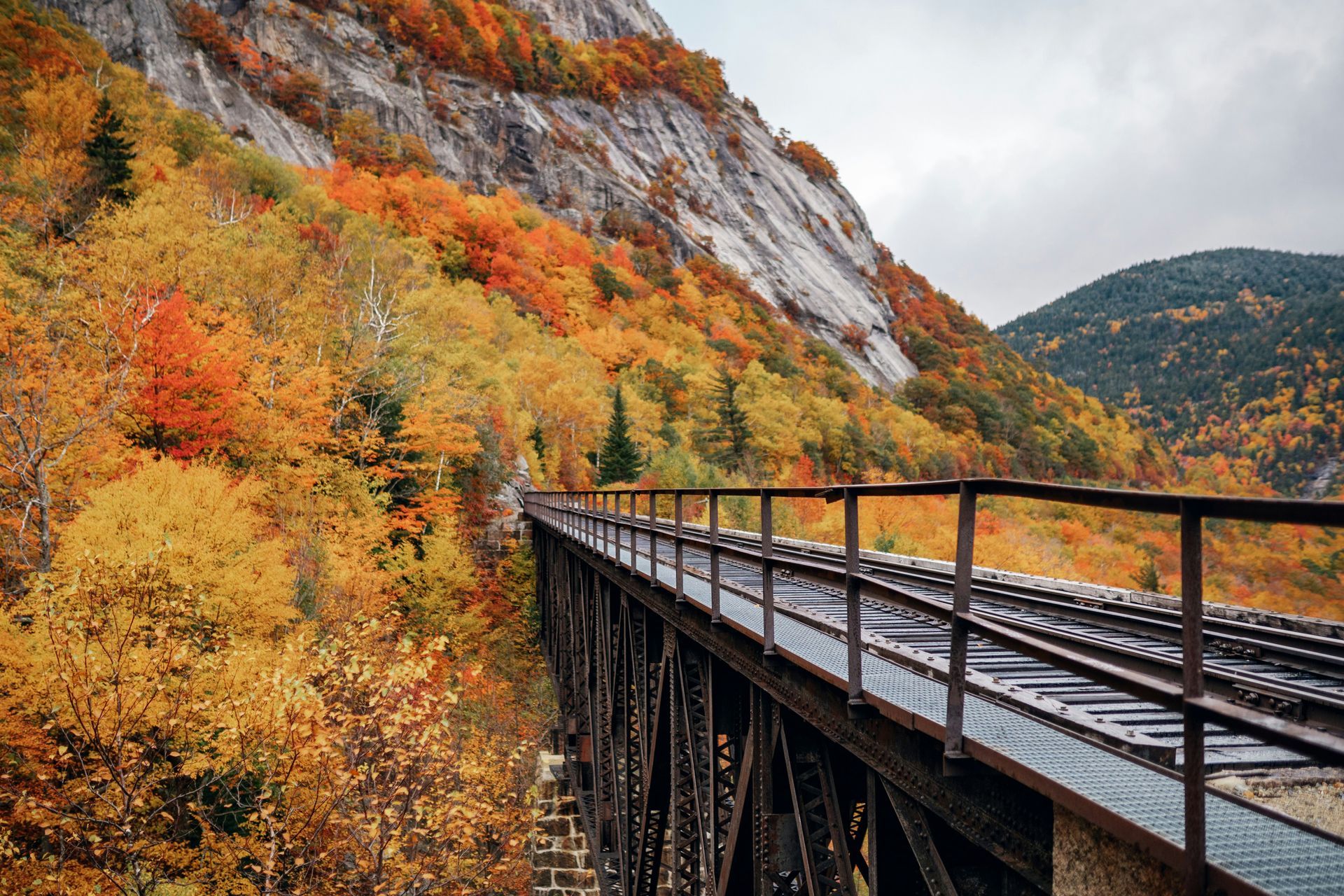 A train bridge in the mountains with autumn leaves on the trees.