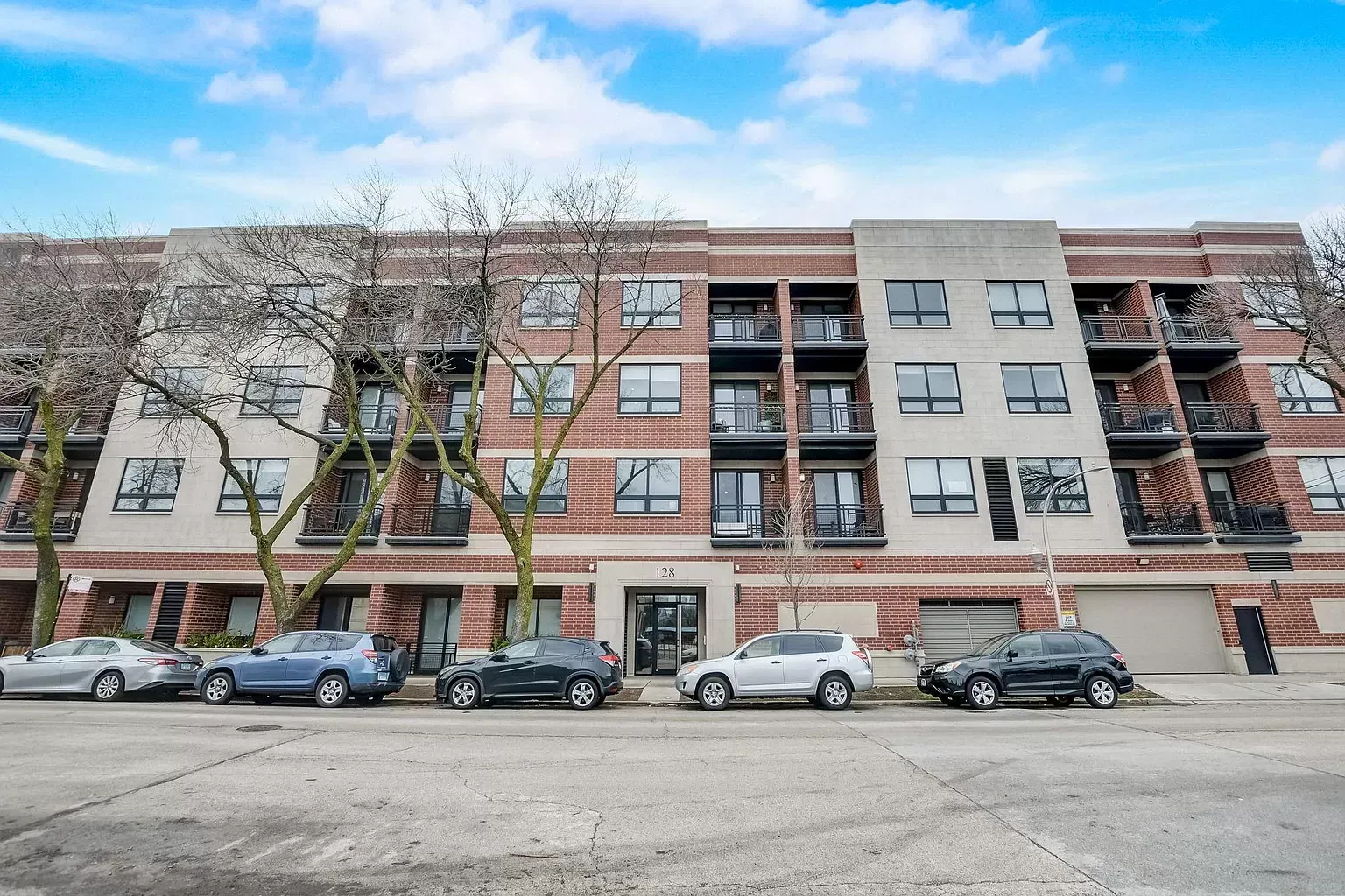 a row of cars are parked in front of a large apartment building .