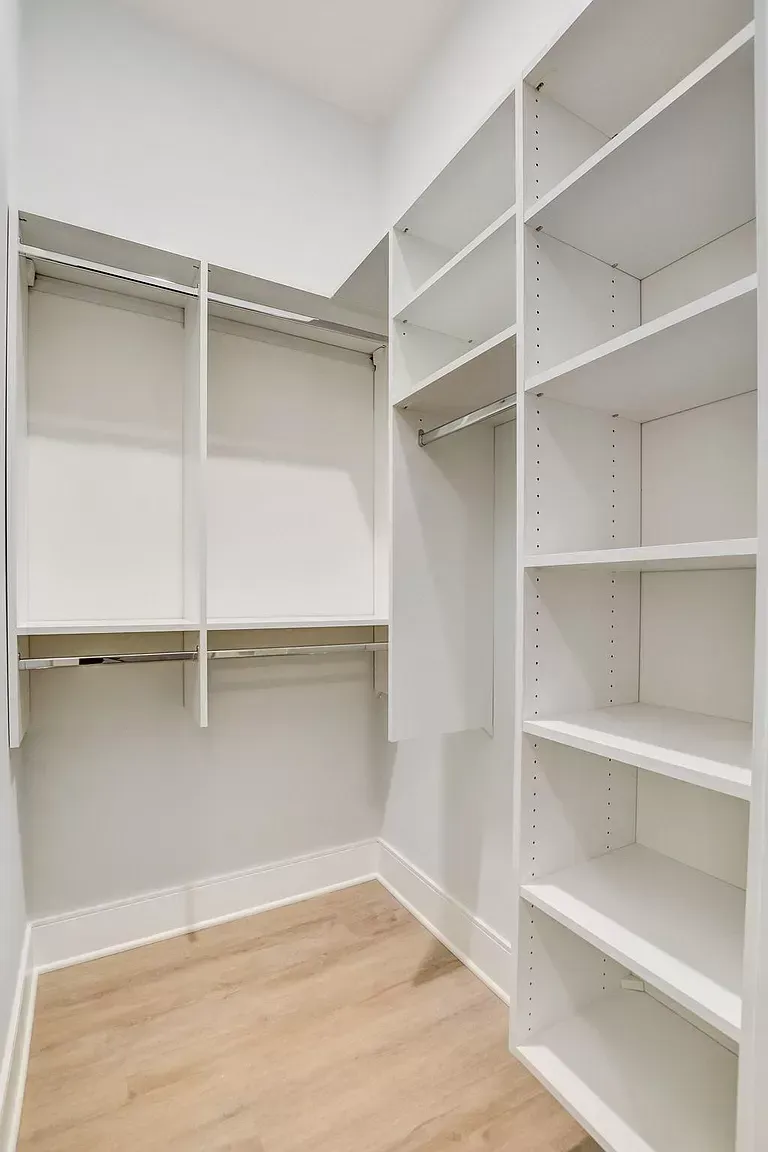 a walk in closet with white shelves and wooden floors .