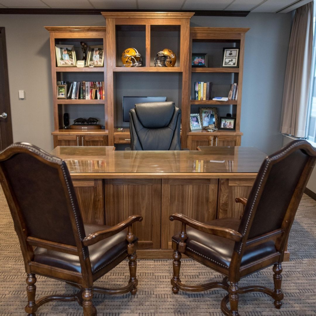 Wood-paneled office with a desk, leather chair, bookcases, and two guest chairs facing it.