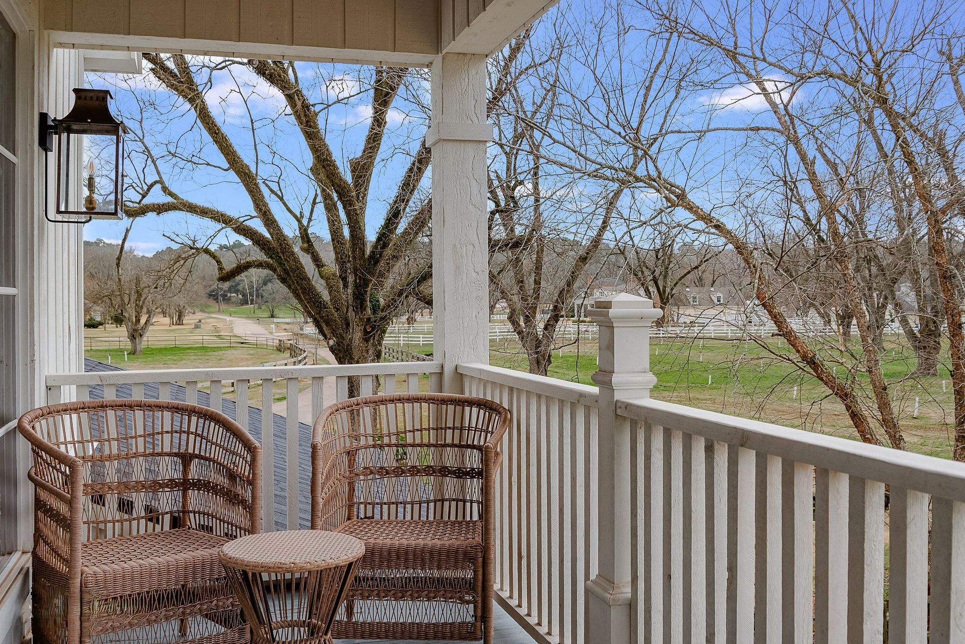 Porch with wicker chairs overlooking a yard with trees and a grassy field