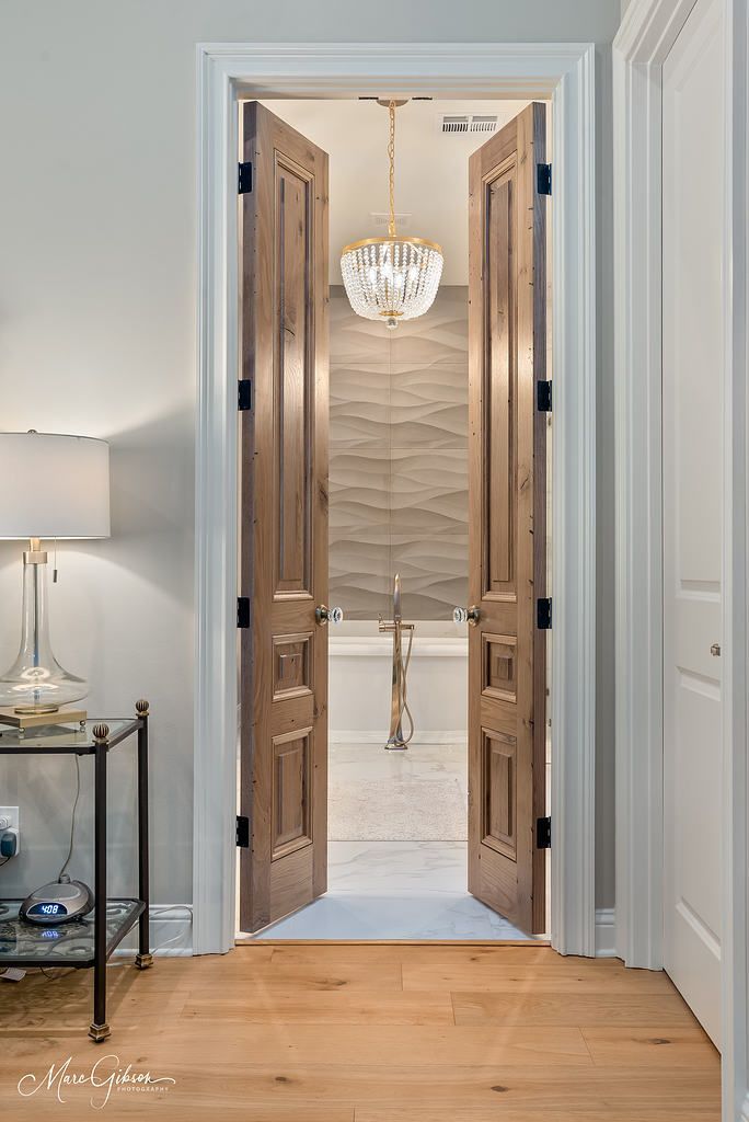 Open double doors leading to a bright room with a chandelier and textured wall accent