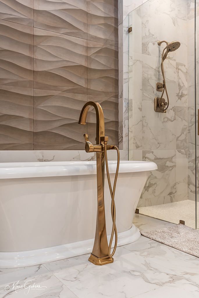 Elegant bathroom with a white freestanding tub, gold faucet, and marble shower wall.