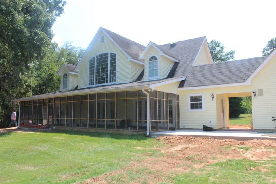 Yellow house with a screened porch and large gable windows, surrounded by trees and grass