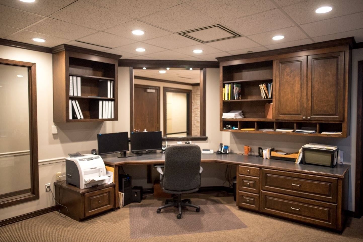 Professional office interior with dark wood desks, cabinets, and a central chair under recessed lighting