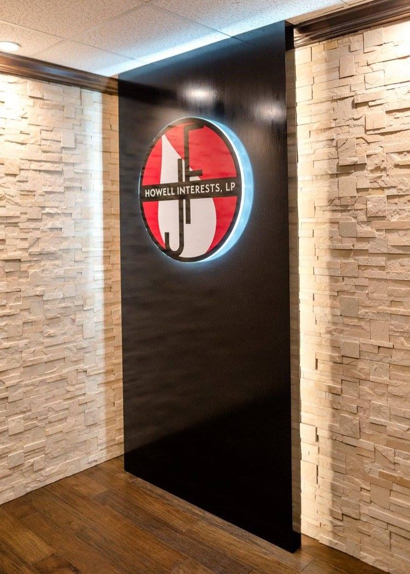 Hallway wall with a black panel and a red-and-white circular logo, between stone-textured walls and wood flooring