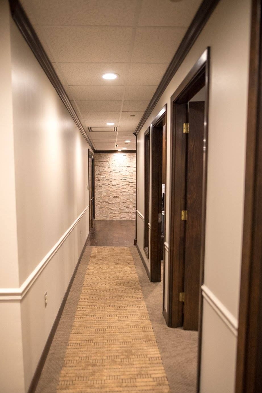 Empty beige hallway with recessed lights, carpet, and several open dark wood doorways