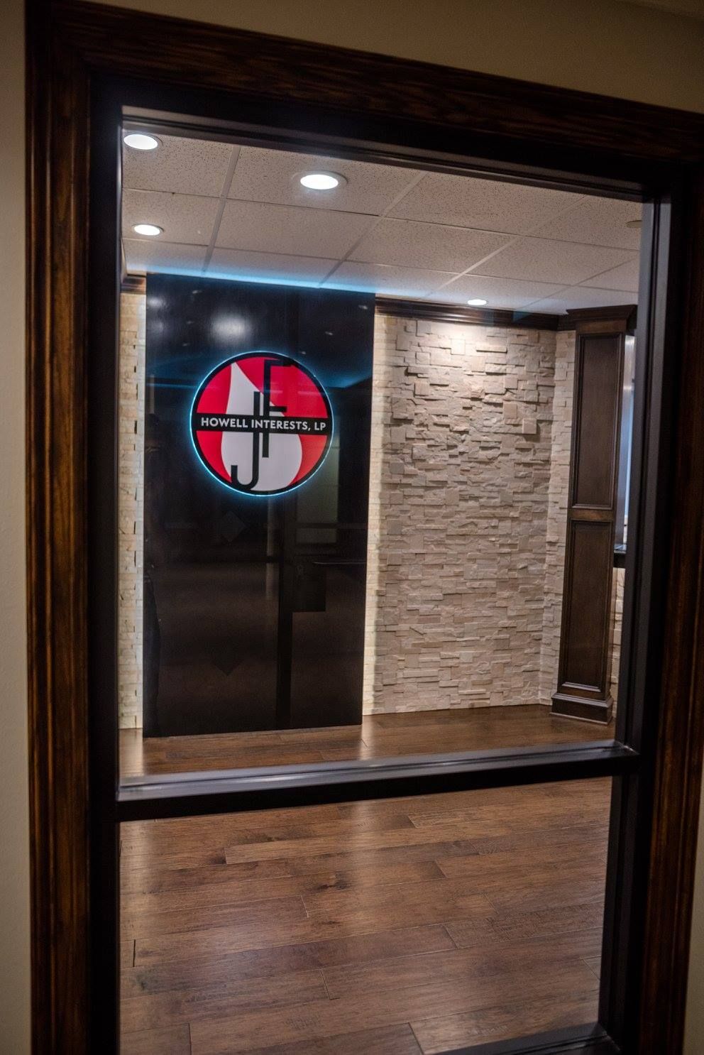 Glass window into a lobby with a circular red, white, and black logo on a brick wall.