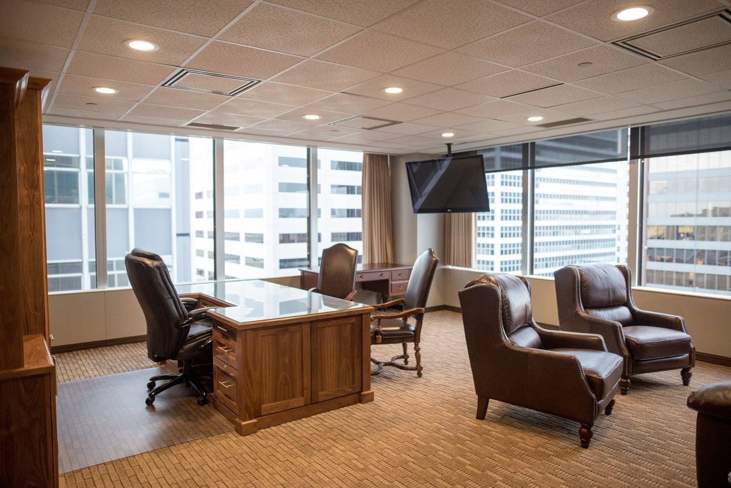 Modern office lounge with leather chairs, wooden desk, and city views through large windows