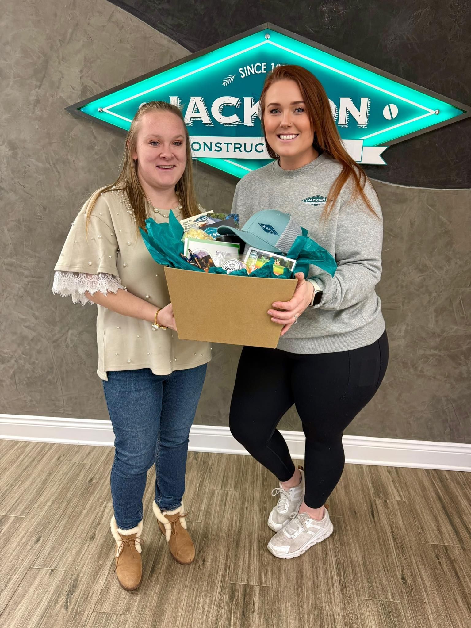 Two people holding a box of gifts in front of a Back to School sign.