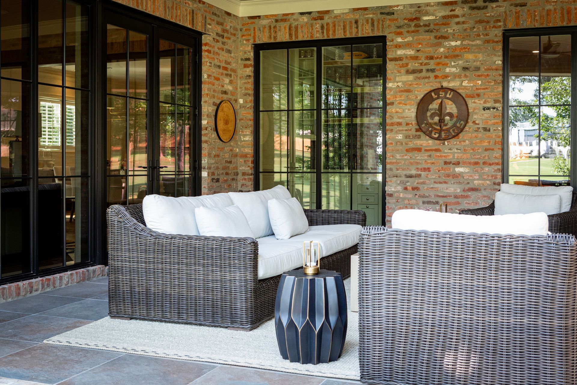 Brick patio with wicker sofas, white cushions, and black side table outside glass doors