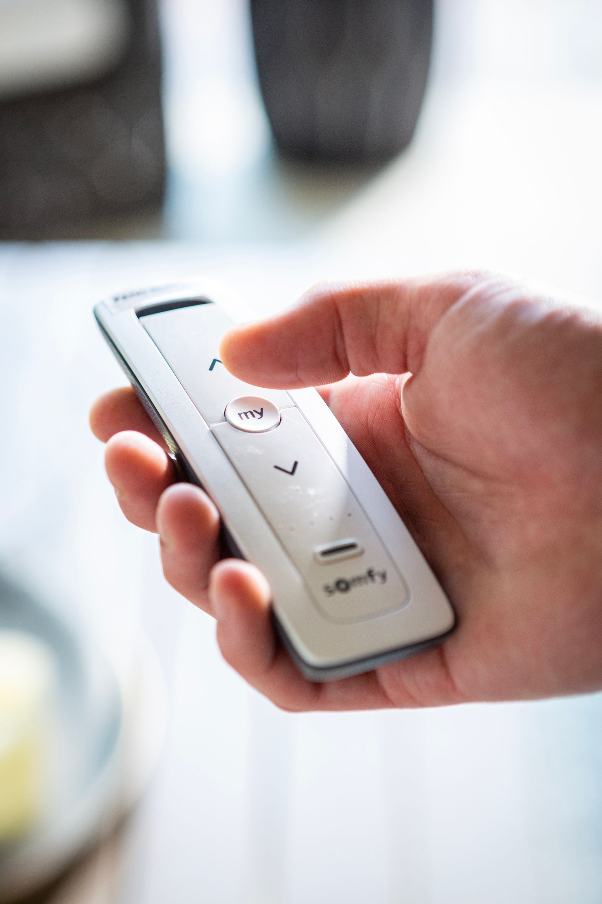 Hand holding a white remote control with a thumb pressing a button