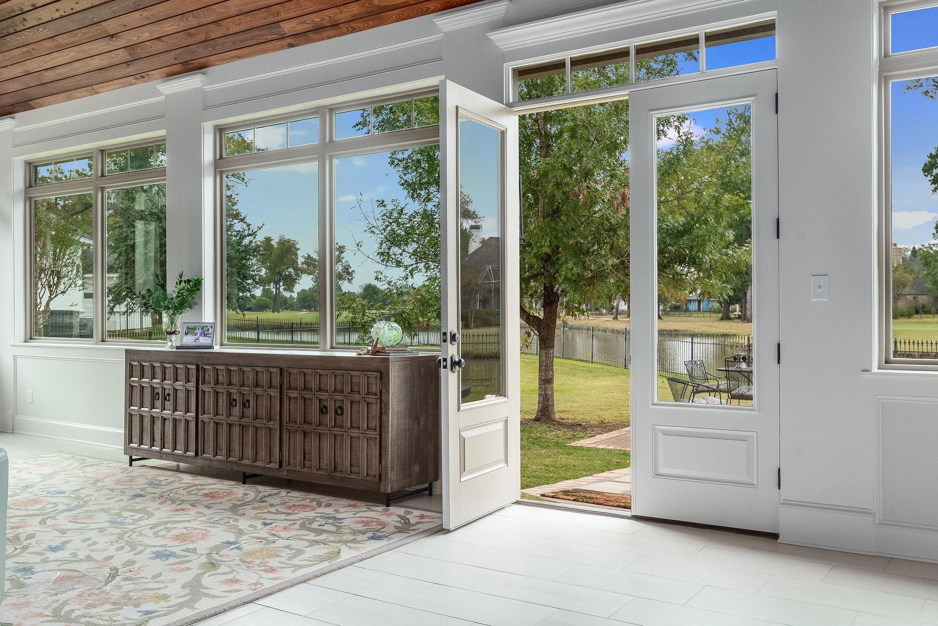 Bright open room with large windows, wooden cabinet, and open glass door to a sunny garden