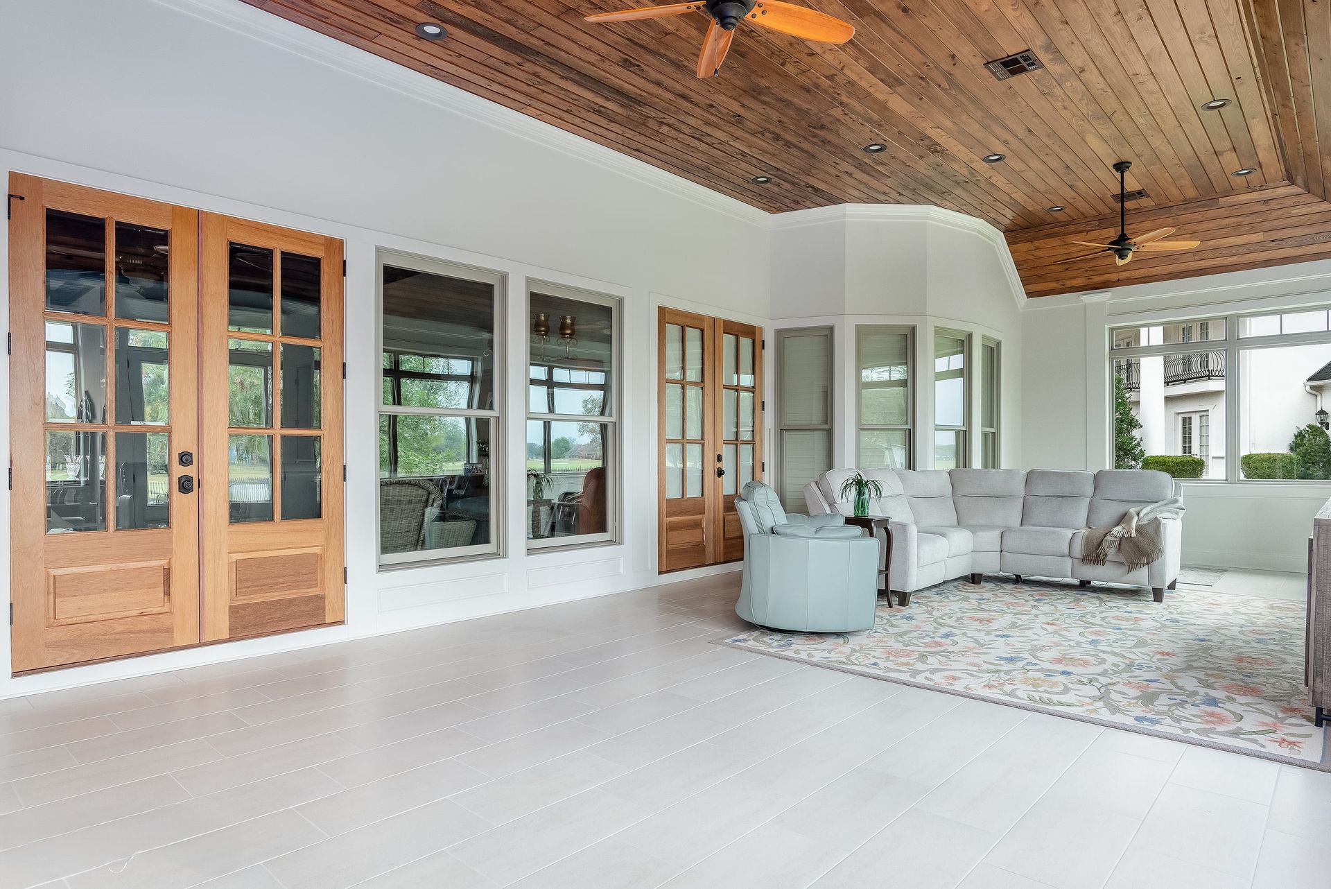 Bright modern sunroom with white walls, wood doors, large windows, gray seating, and a woven ceiling
