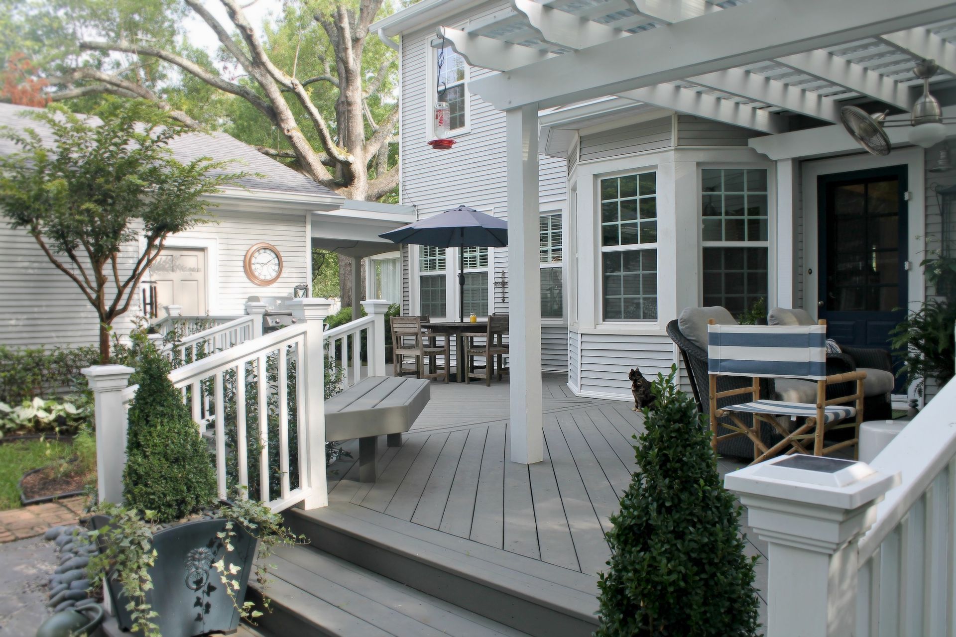 White house porch with gray deck, railings, outdoor chairs, and potted greenery.