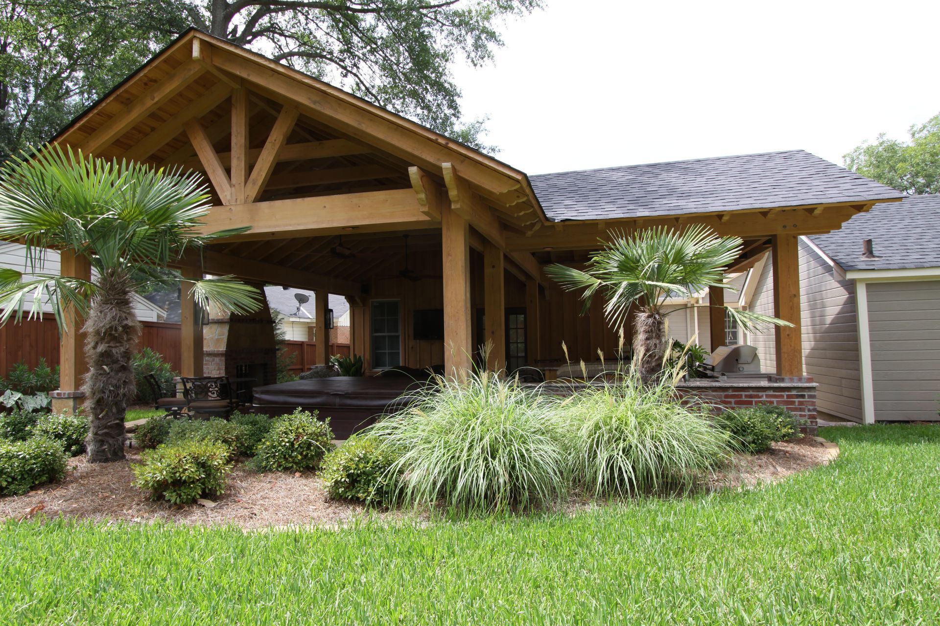 Wooden house porch with stone columns, palm trees, and landscaped front yard