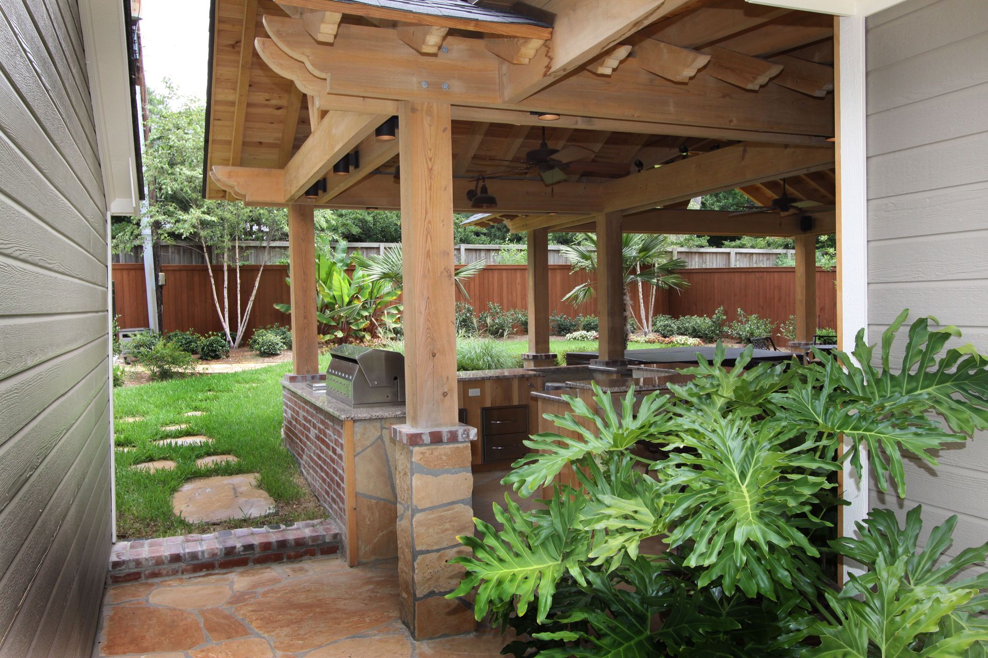 Covered outdoor patio with damaged wooden roof, stone column, and green plants beside a house