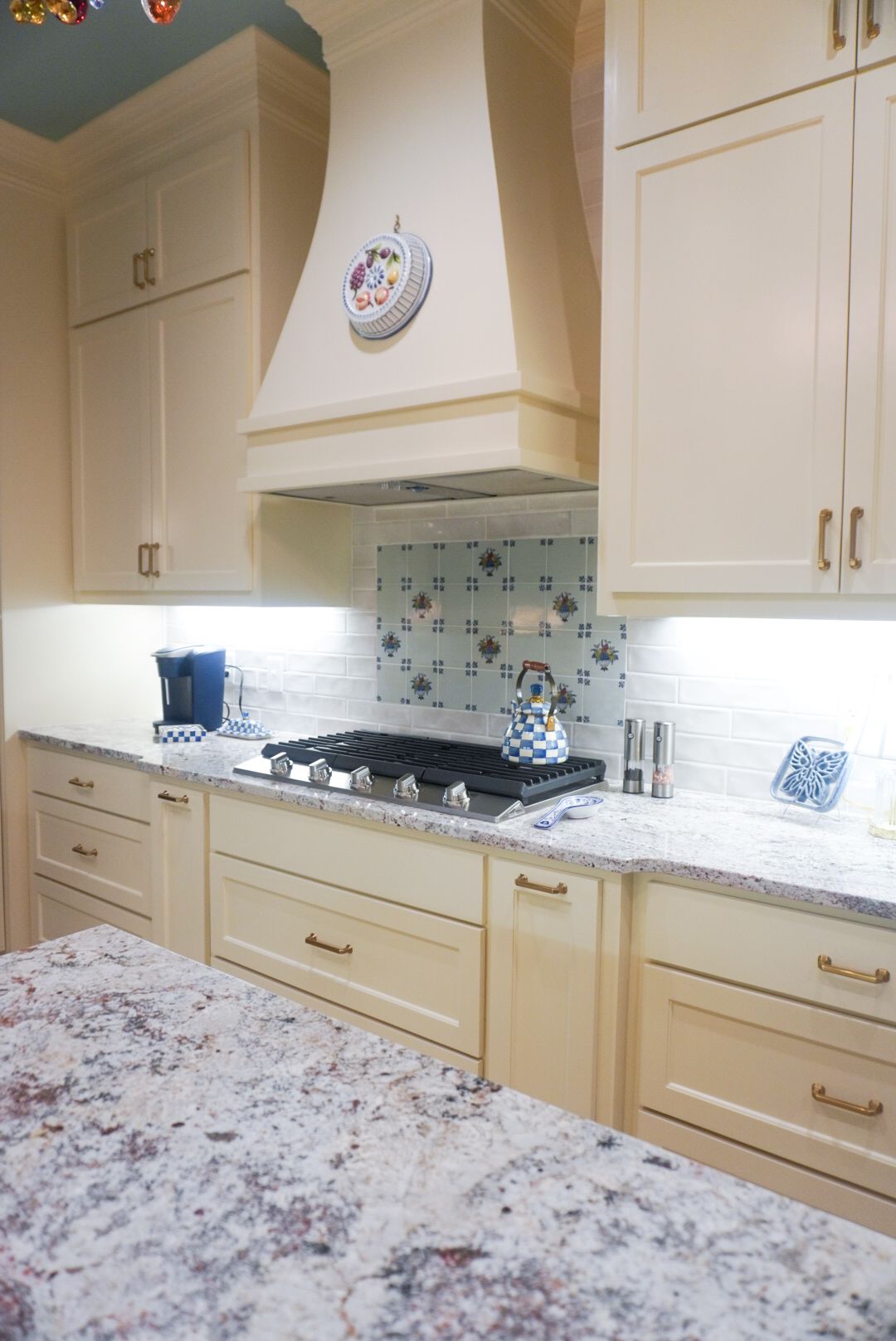 Cream kitchen with marble island, beige cabinets, and a gas cooktop under a decorative hood.