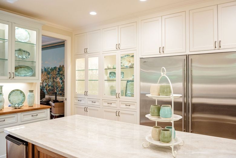 Bright kitchen with white cabinets, marble island, and glass display shelves with pastel decor