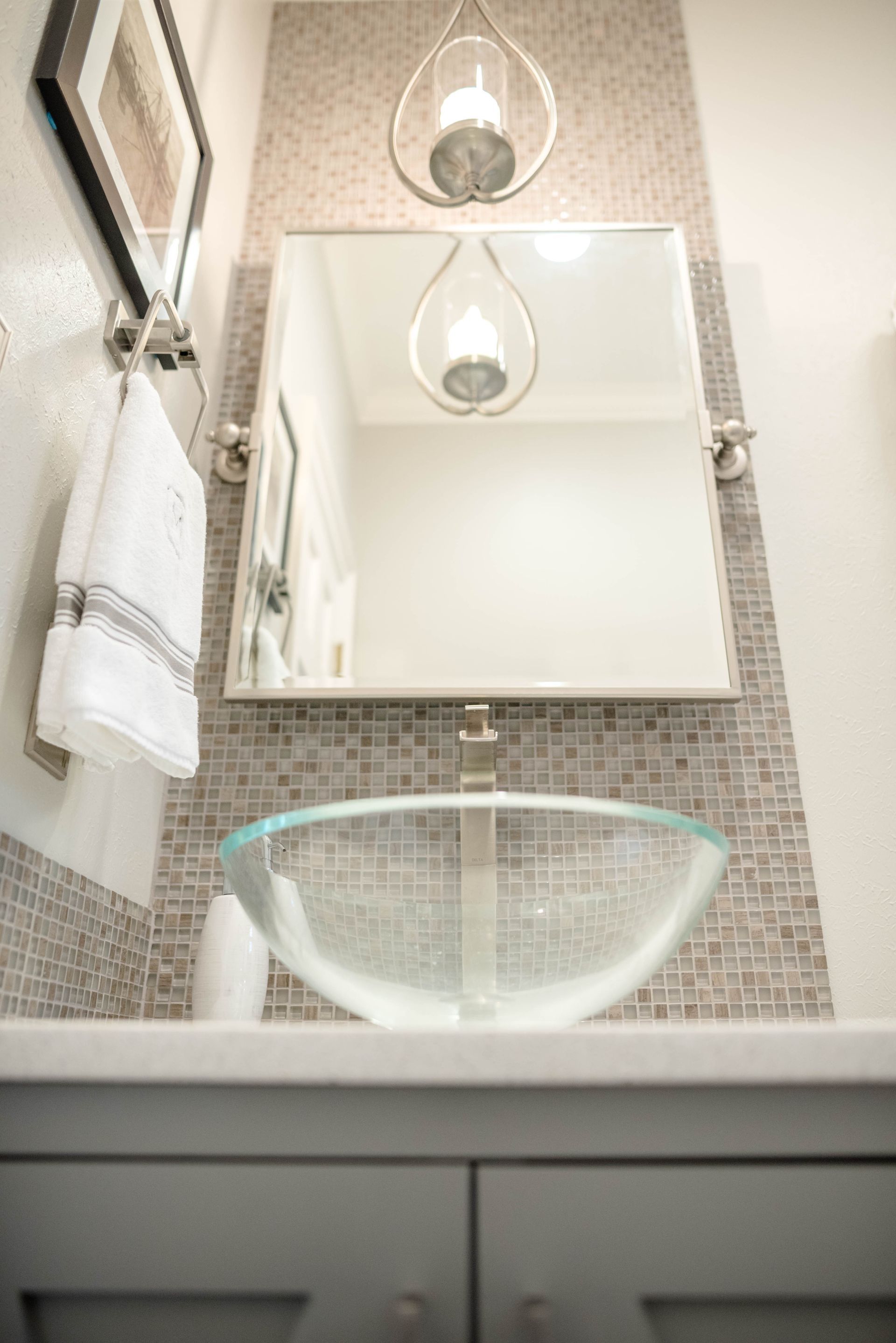 Modern bathroom with mosaic-tiled wall, mirror, glass vessel sink, and pendant light fixtures