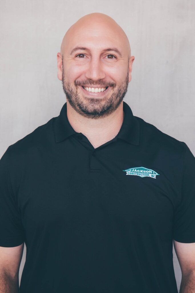 Smiling bald man in a black polo shirt against a light gray background
