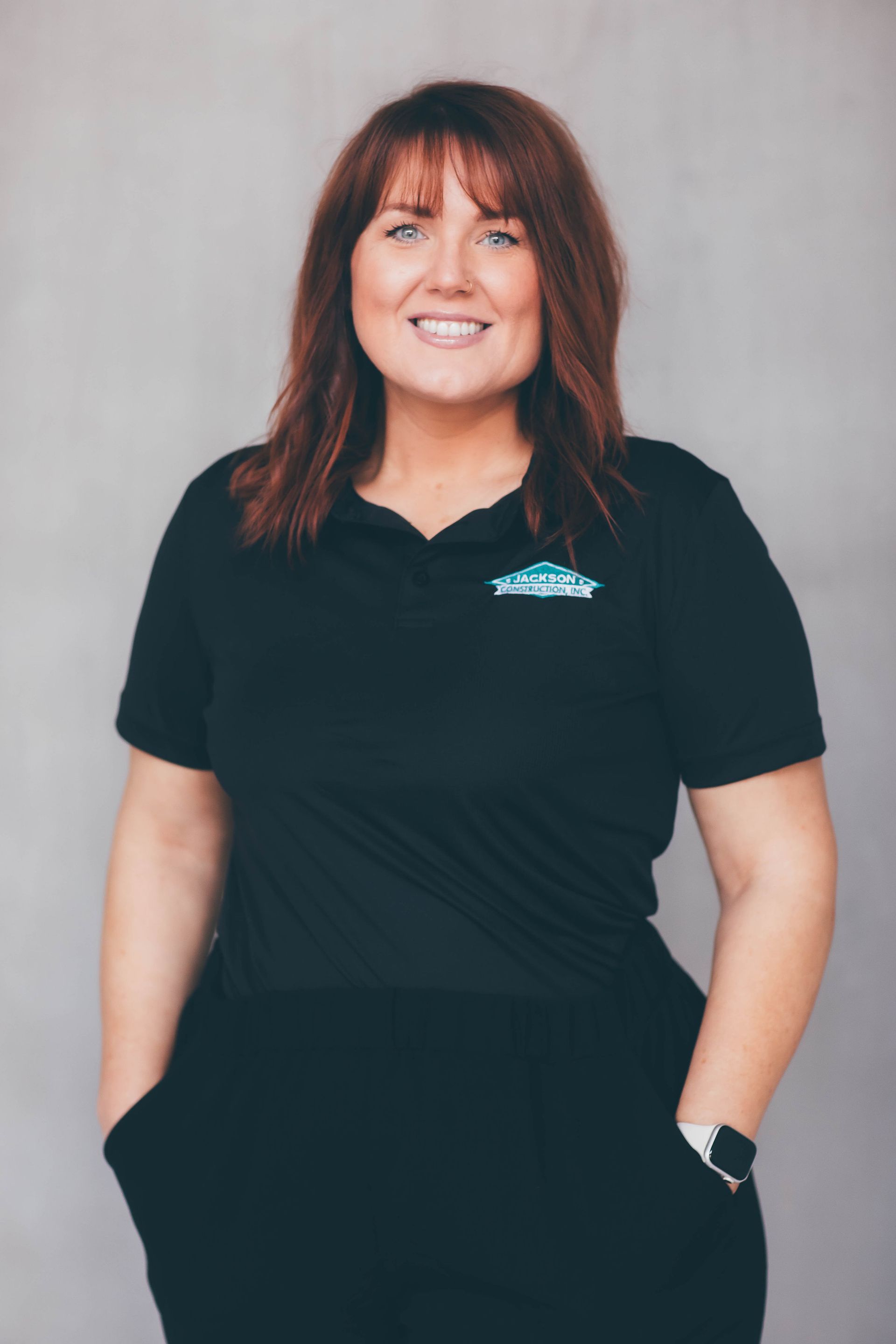 Smiling woman in a black polo shirt standing against a light gray background