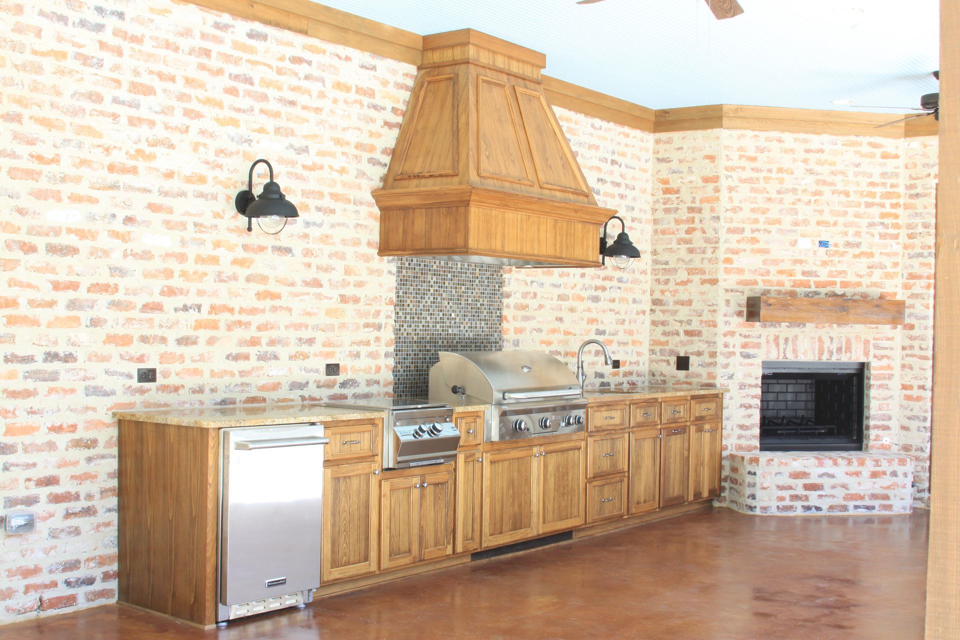 Brick-lined kitchen with wooden cabinets, stainless appliances, and a large copper range hood